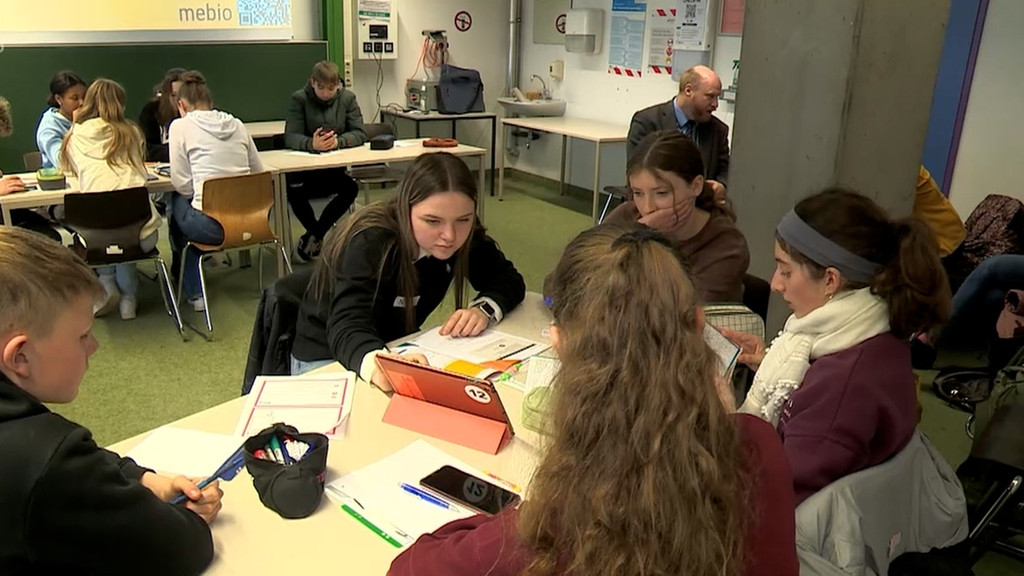 In einem Klassenzimmer sitzen Schülerinnen und Schüler an ihren Plätzen und schauen in Tablets. 