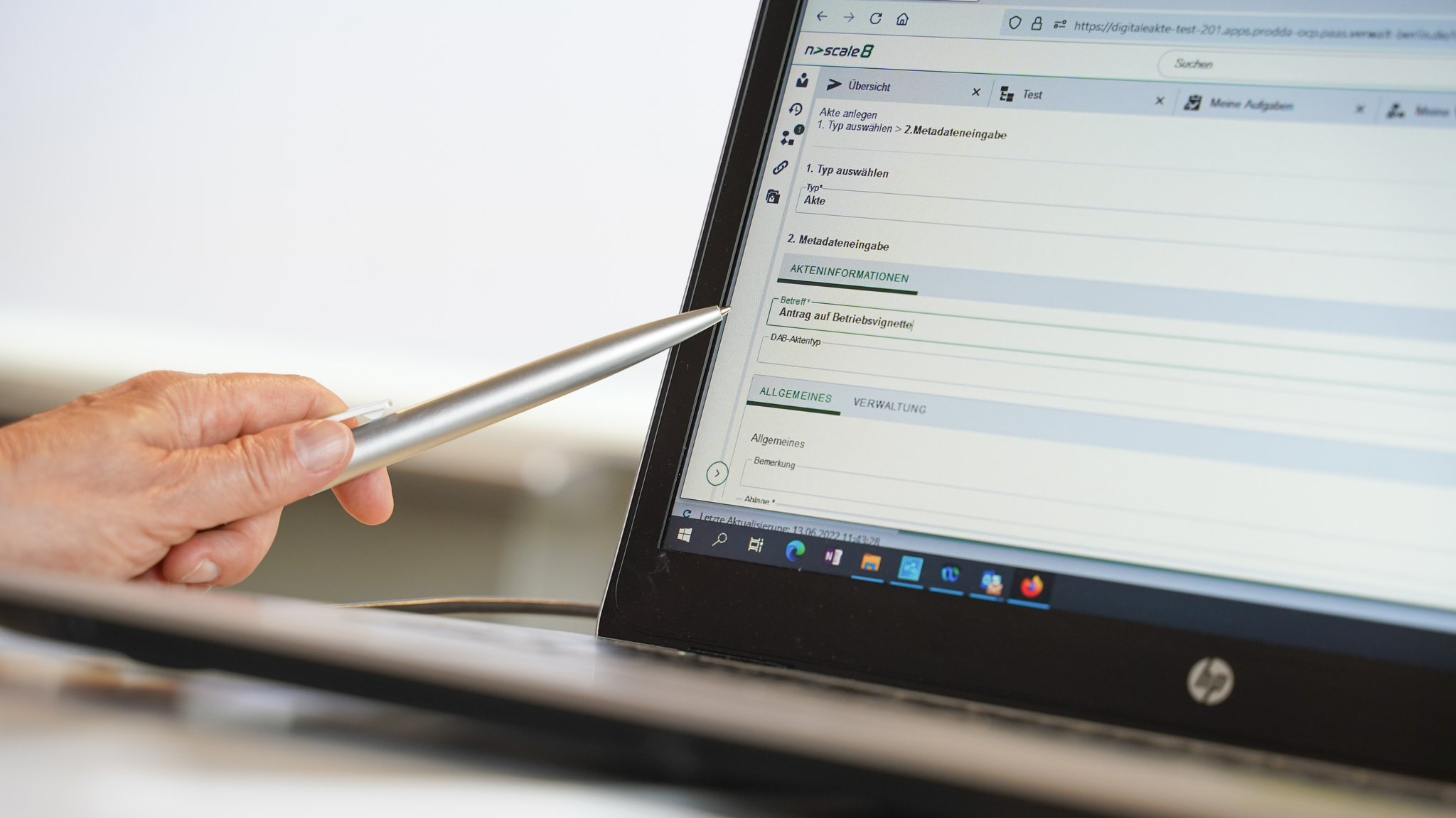 Eine Frauenhand zeigt mit einem Kugelschreiber auf einen Computer, auf dem eine Eingabemaske zu sehen ist. 