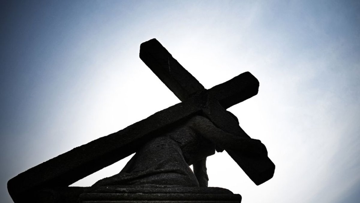 Symbolbild: Gegen die Sonne zeichnet sich eine Jesusstatue unter dem Kreuz ab.