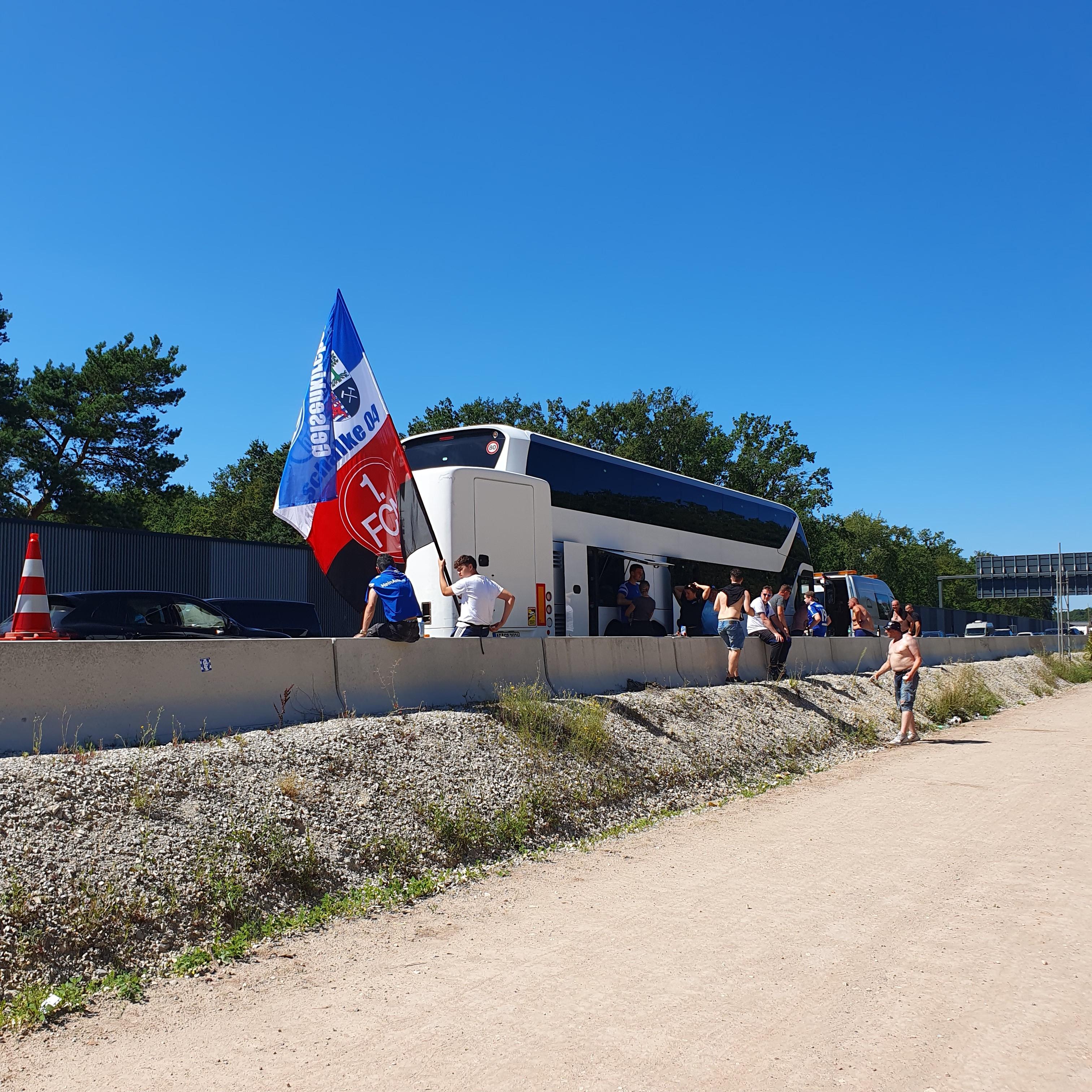 Fußballfans stehen neben einem Reisebus auf der A3. 