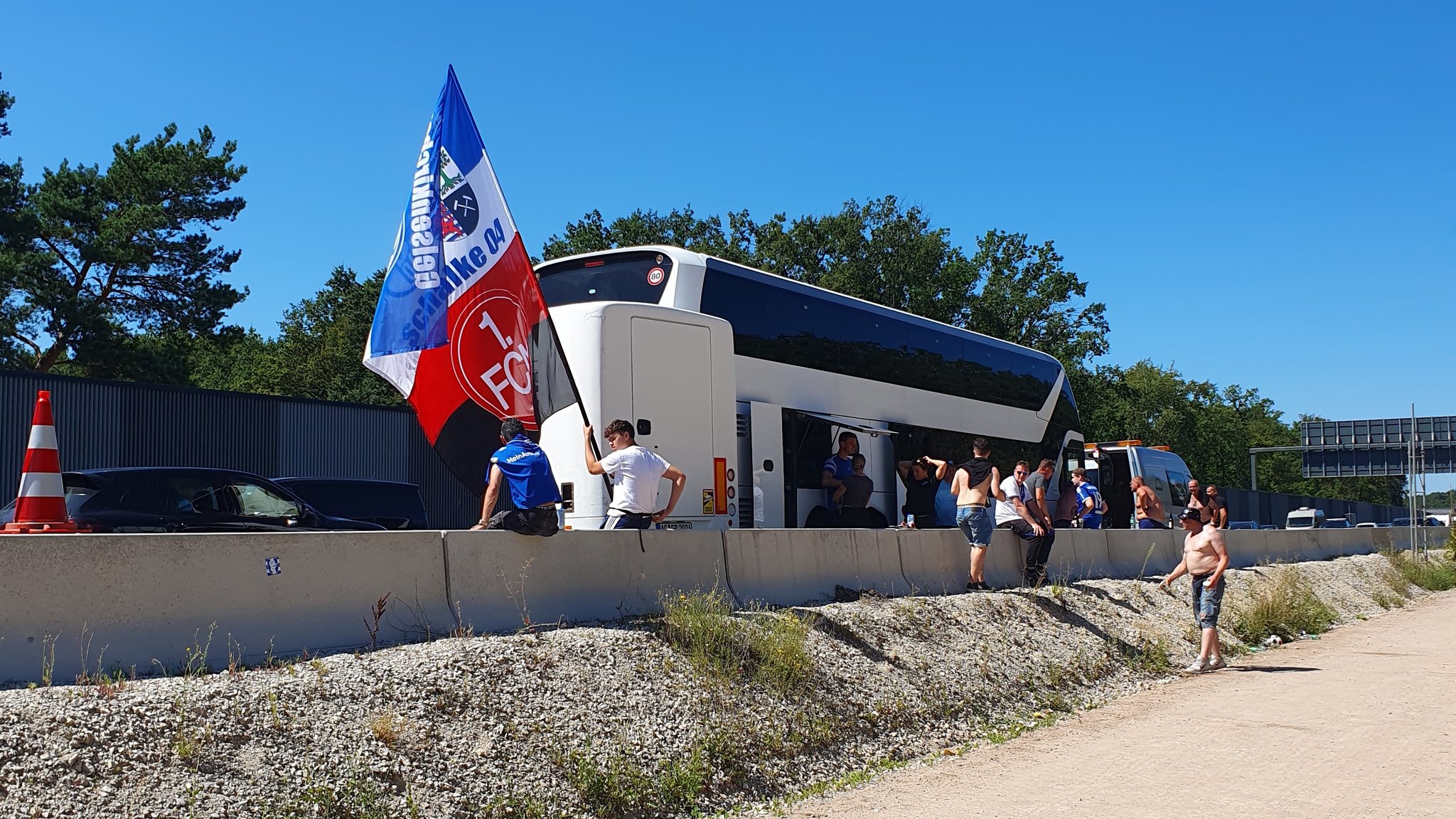 Fußballfans stehen neben einem Reisebus auf der A3. 