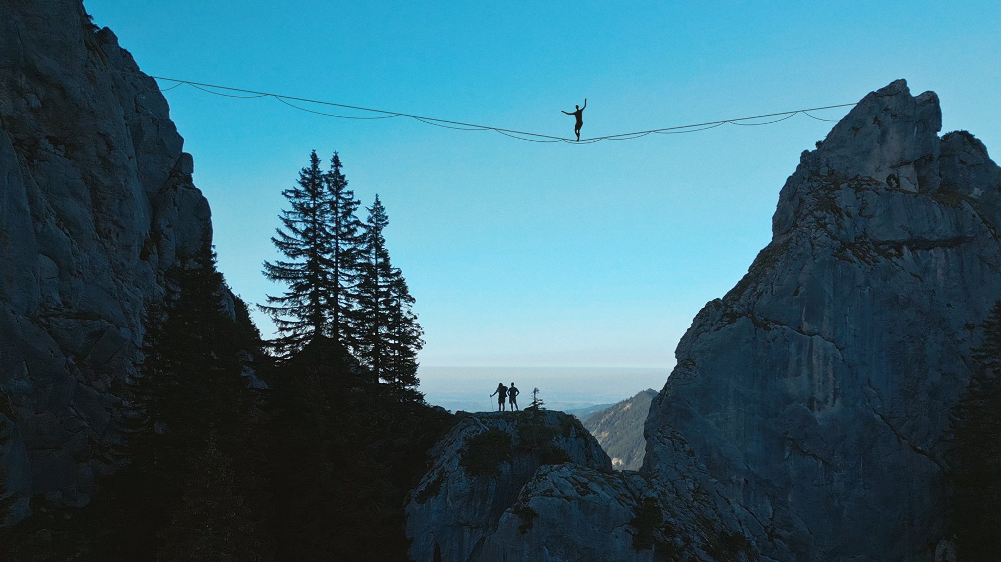 Ein Mann balanciert über eine zwischen zwei Berggipfeln gespannte Highline. 