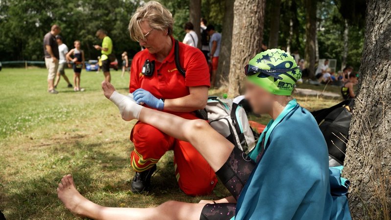 Eine Ersthelferin versorgt den Fuß einer Schwimmerin. | Bild: BR/Michael Böhm Eine Ersthelferin versorgt den Fuß einer Schwimmerin.