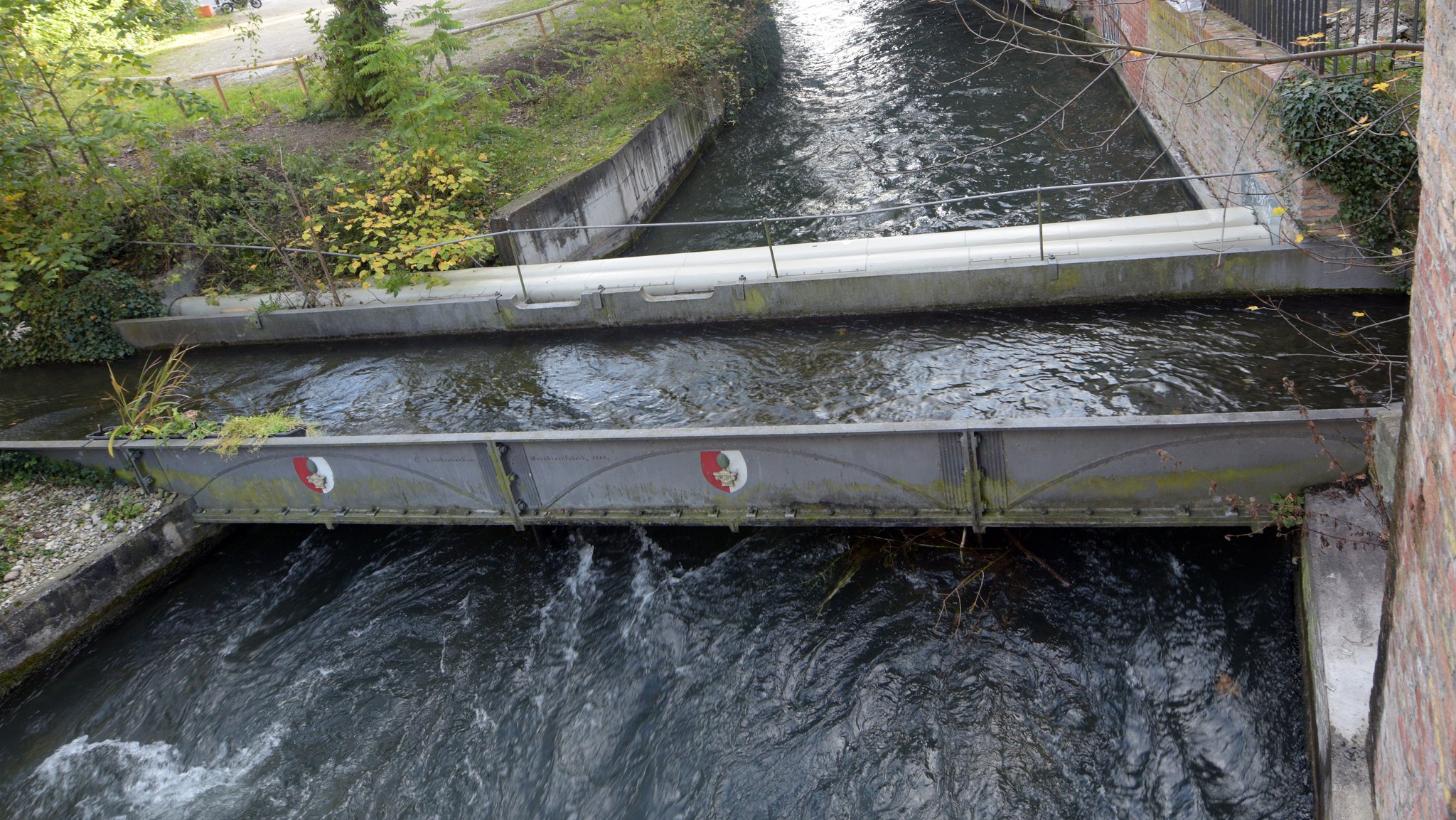 Zwei Kanäle kreuzen sich in Augsburg mithilfe einer Stahlbrücke, auf der das Stadtwappen angebracht ist.