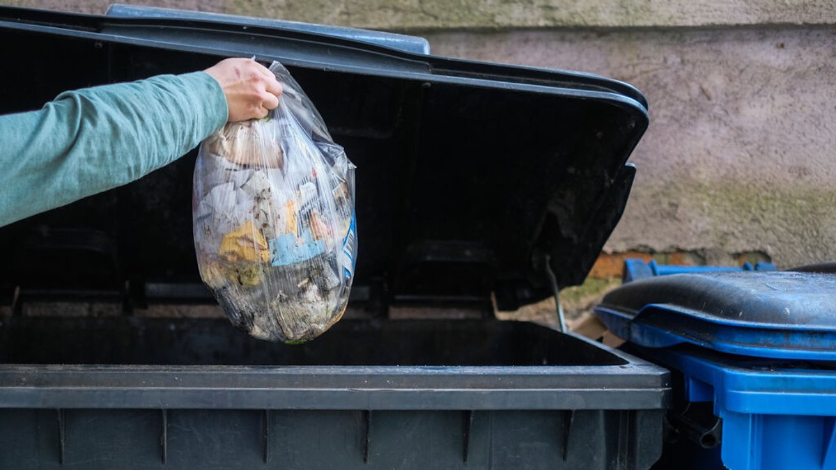 Eine Person wirft einen Müllsack in die Restmüll-Tonne.