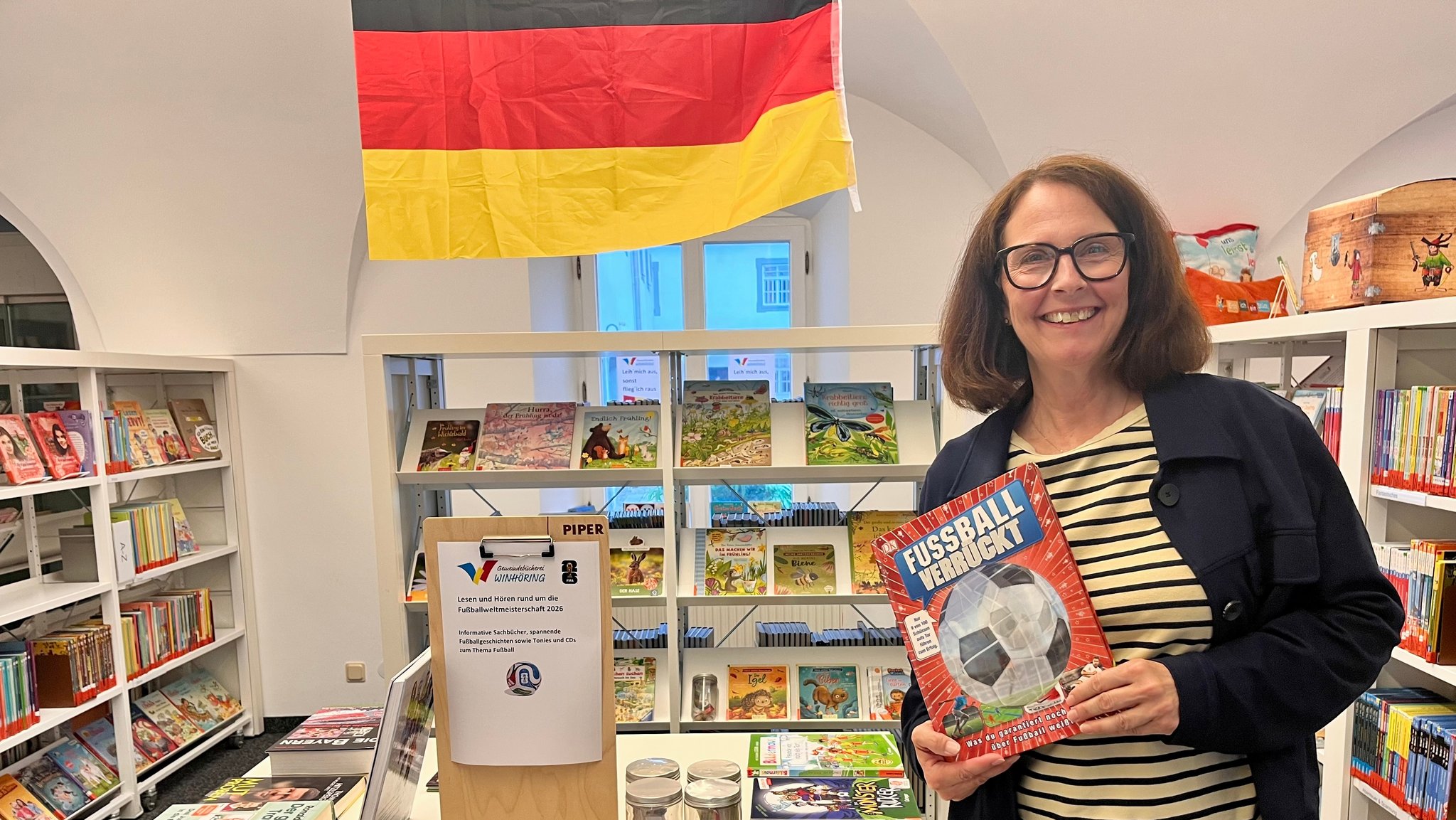Sandra Stubenvoll, Leiterin der Gemeindebücherei in Winhöring. Dahinter ein Aktionstisch zur Fußball-WM mit Hörspielen und Büchern zum Thema. | Bild: BR / Sandra Demmelhuber Sandra Stubenvoll, Leiterin der Gemeindebücherei in Winhöring. Dahinter ein Aktionstisch zur Fußball-WM mit Hörspielen und Büchern zum Thema.