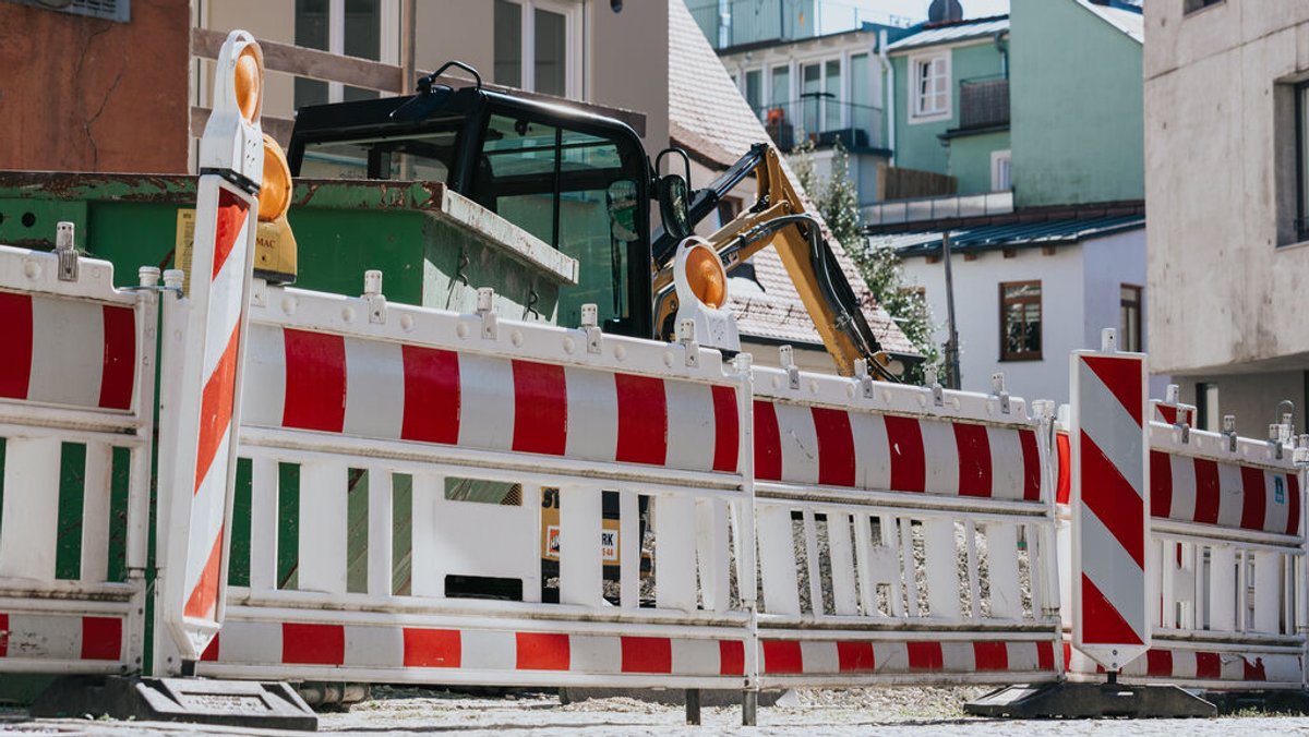 Eine Baustelle mit Absperrungen, einem Container und einem Bagger mitten in einem Wohngebiet.