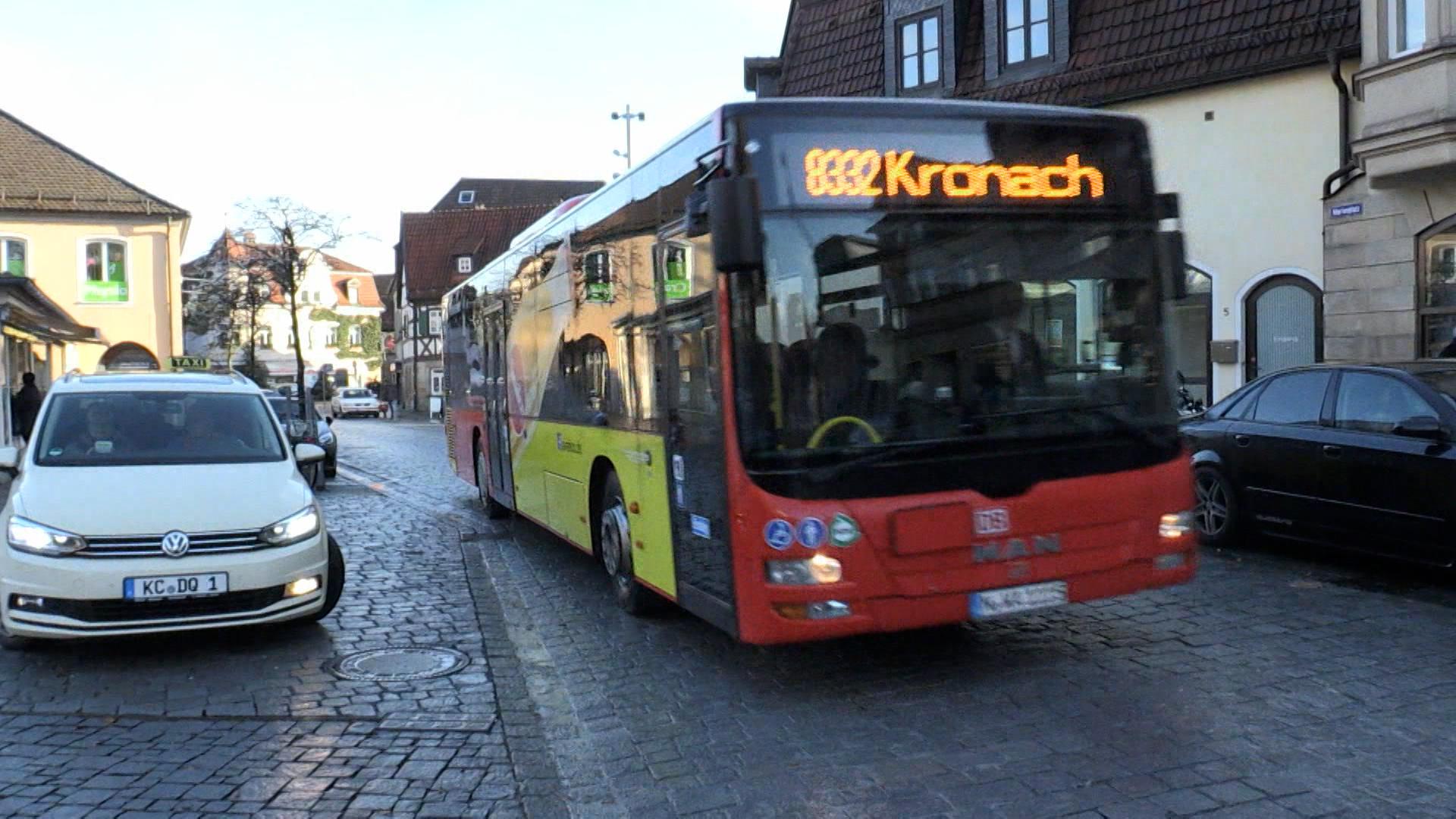 Ein roter Bus, auf dem in gelber Leuchtschrift 8332 Kronach zu lesen ist, fährt durch einen Ort.