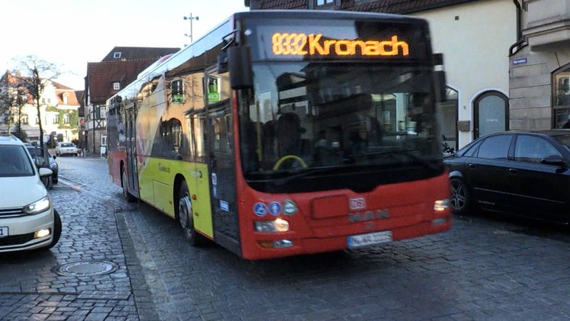 Ein roter Bus, auf dem in gelber Leuchtschrift 8332 Kronach zu lesen ist, fährt durch einen Ort.