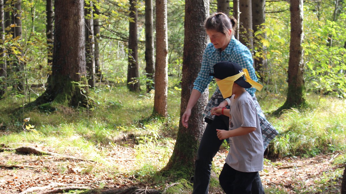 Eine Betreuerin führt ein Kind mit verbundenen Augen durch den Wald 