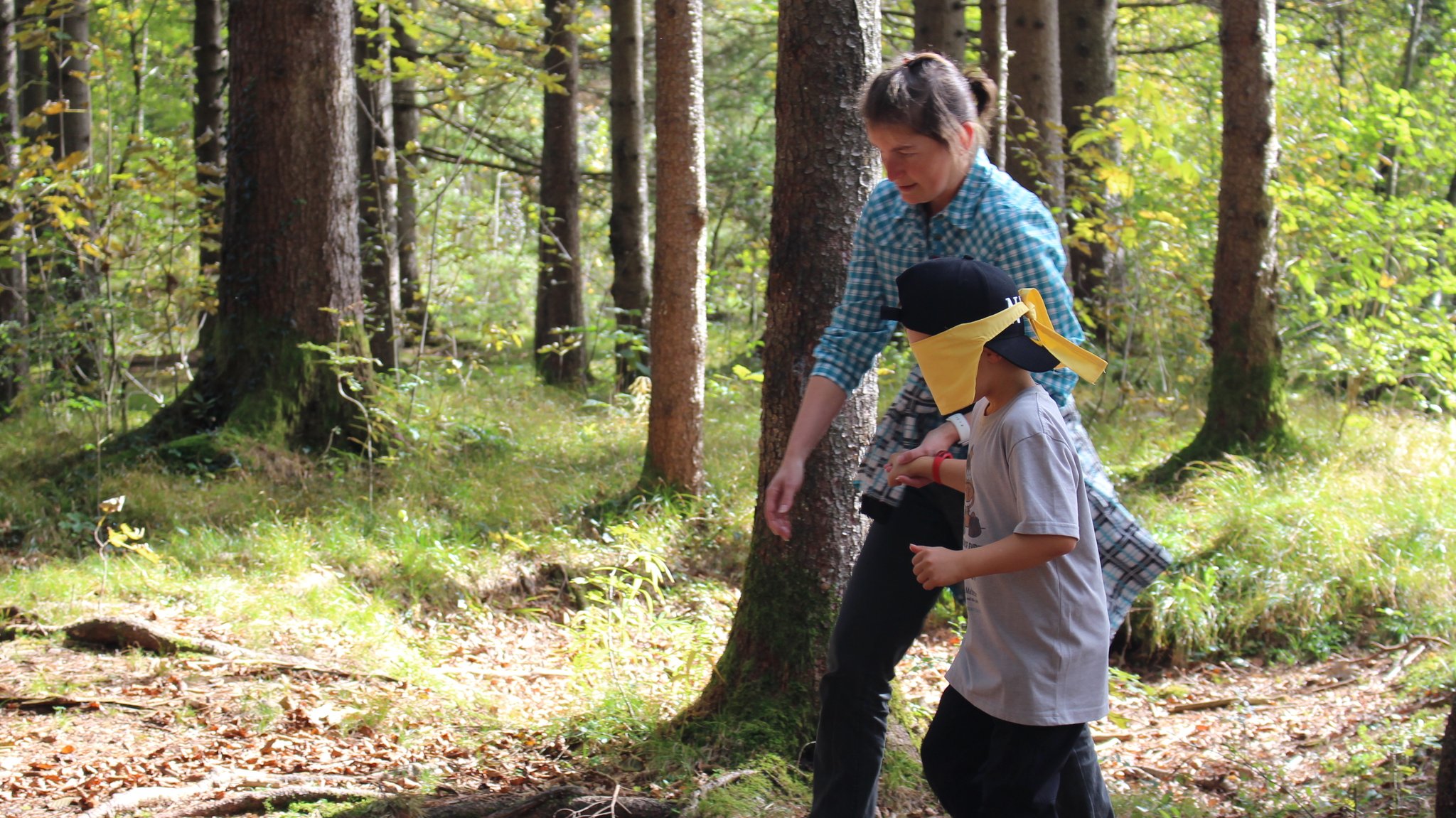 Eine Betreuerin führt ein Kind mit verbundenen Augen durch den Wald 