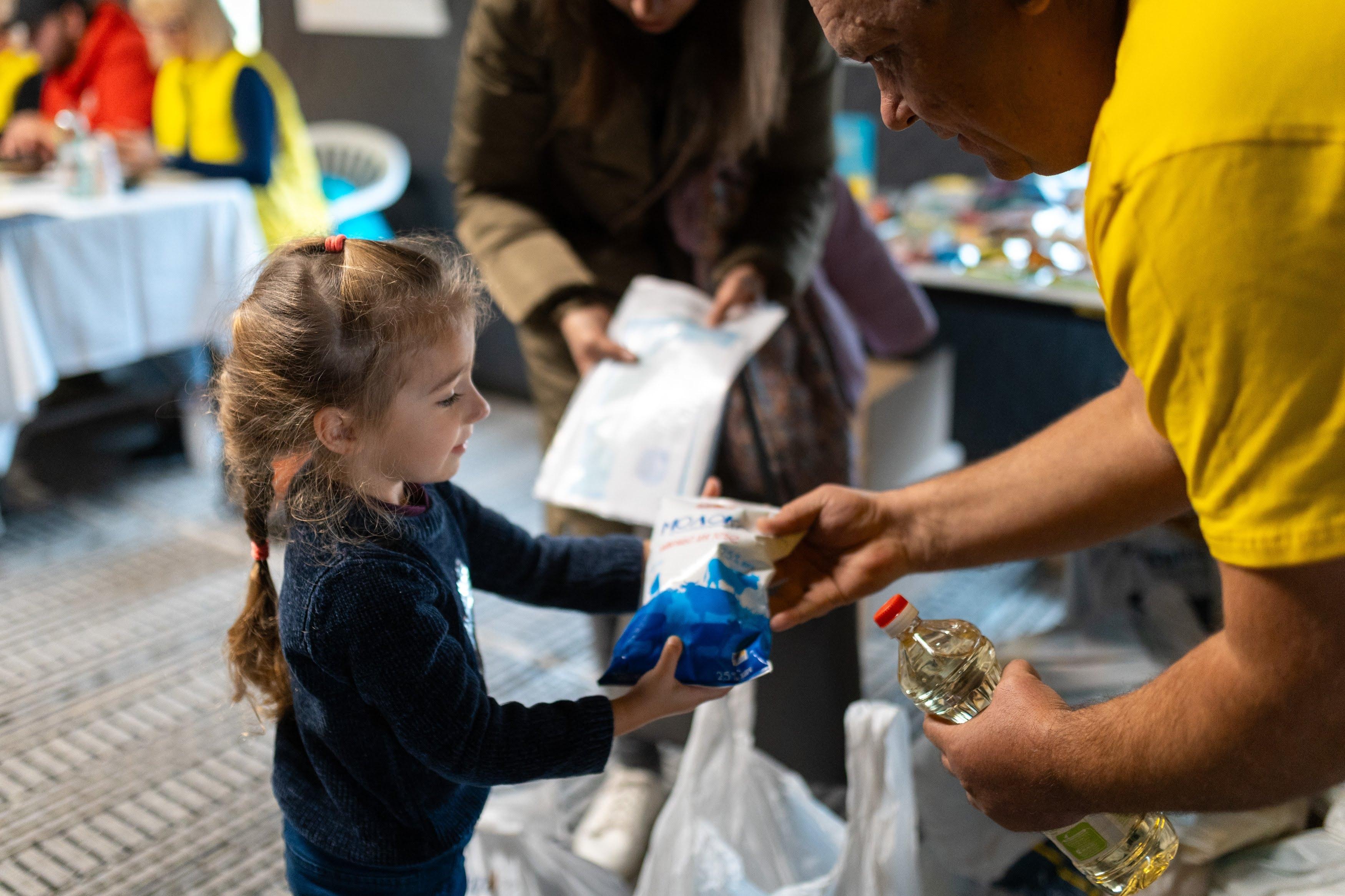 Ein kleines Mädchen erhält an einem Wärmepunkt für Binnengeflüchtete ein Paket Zucker und eine Flasche Öl.