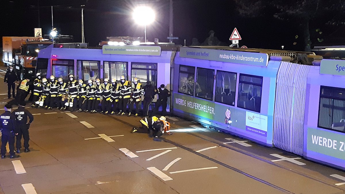 Mitarbeiter der Feuerwehr versuchen Straßenbahn wieder ins Gleis zu schieben