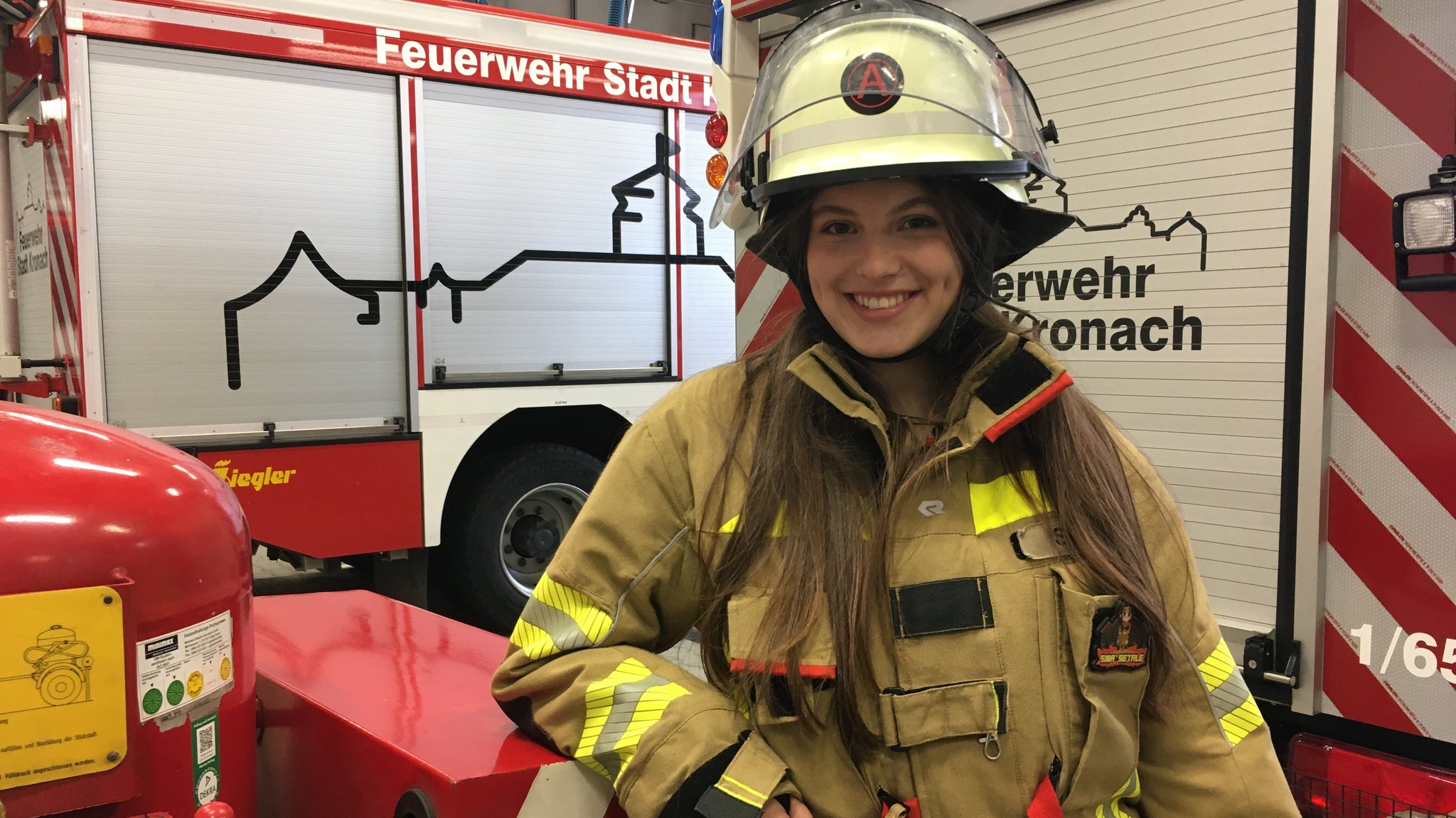 Sina Setale in Feuerwehrkleidung vor zwei Einsatzfahrzeigen der FFW Kronach. 