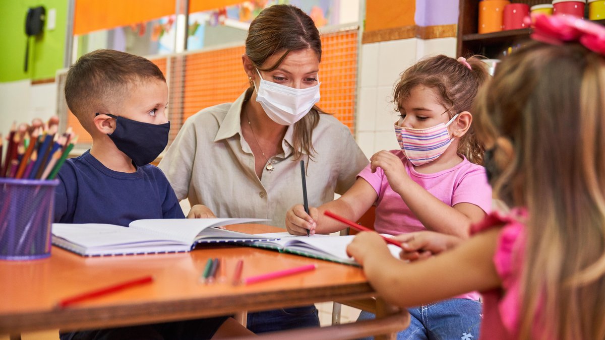 Kinder und Erzieherin in Kita mit Mundschutz wegen der Corona-Pandemie.