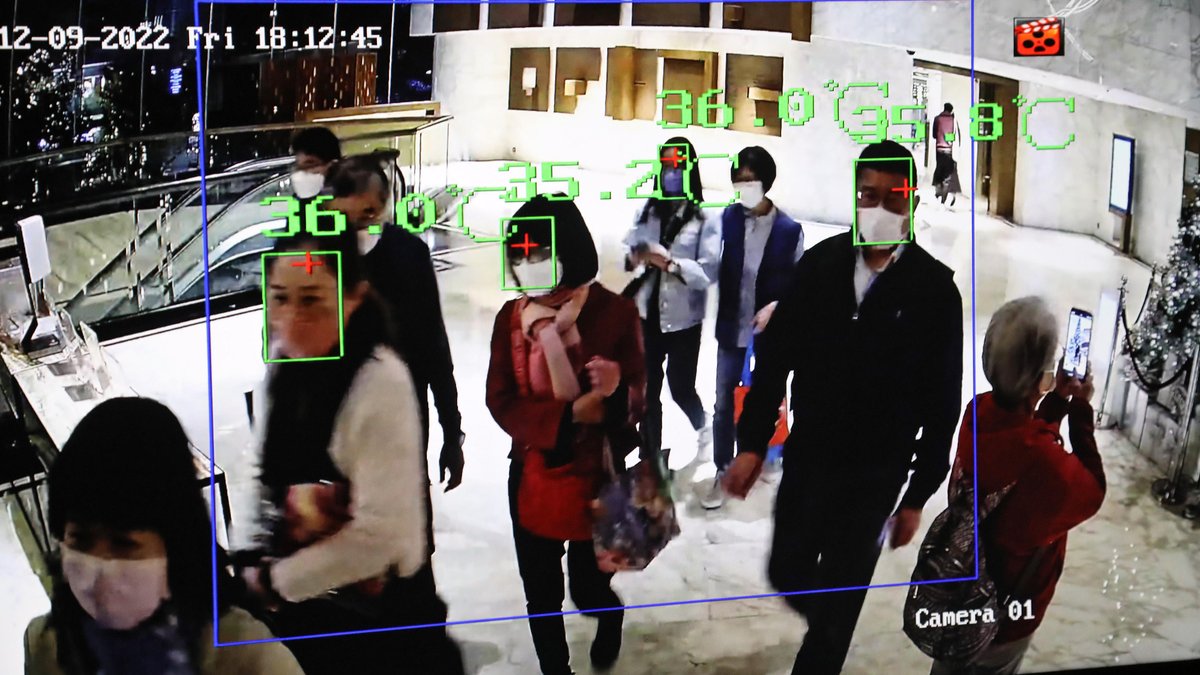 Ein Monitor zeigt die aktuelle Körpertemperatur von Hotelgästen in einer Lobby in Hongkong an. Ein Algorithmus trackt die Gesichter der Gäste mit einem grünen Rahmen.