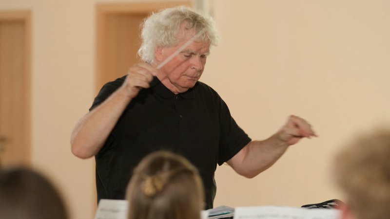 Simon Rattle dirigiert bayerische Blasmusikgruppen.