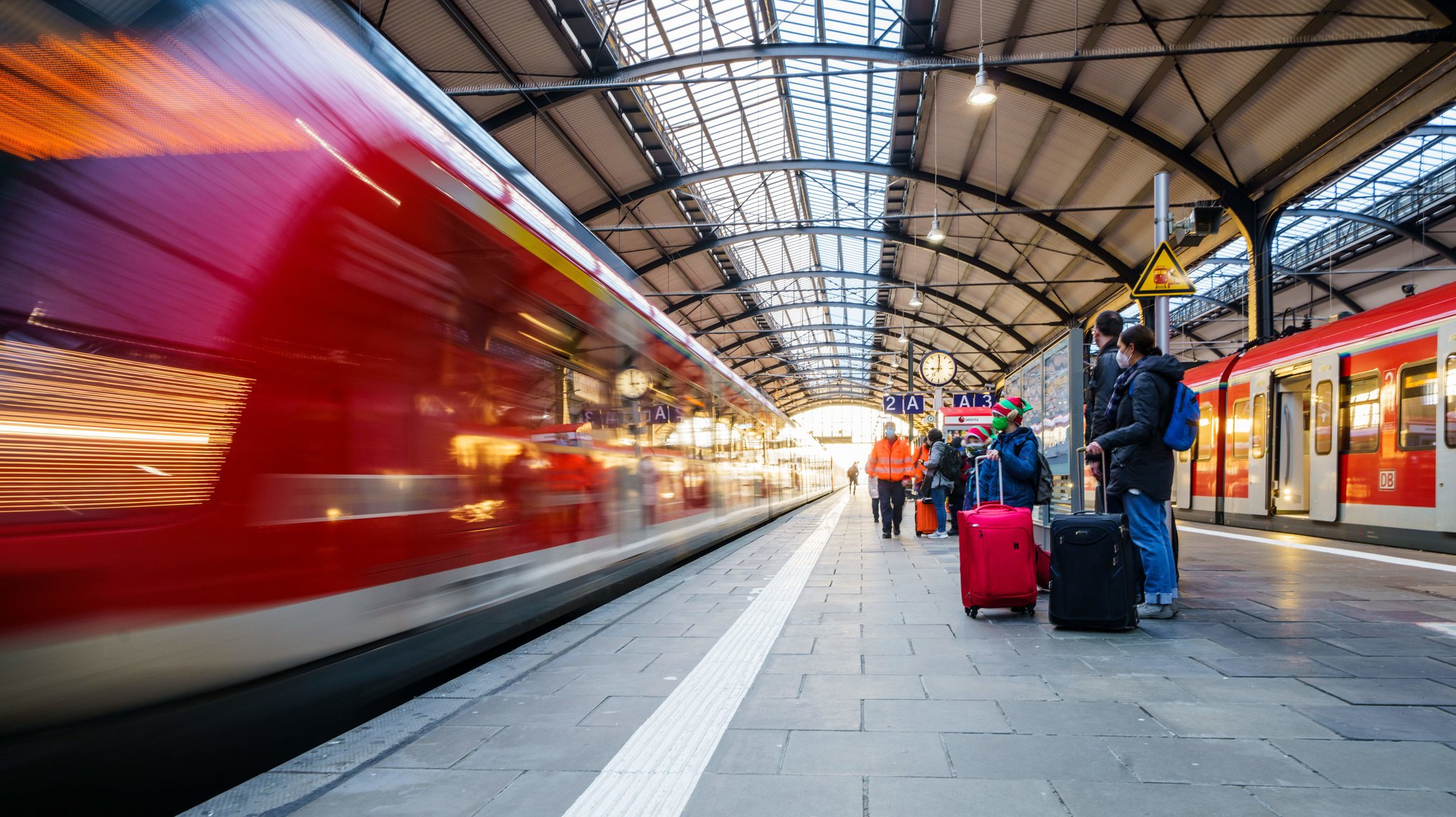 Bahnreisende stehen auf dem Bahnsteig während ein Regionalzug einfährt.