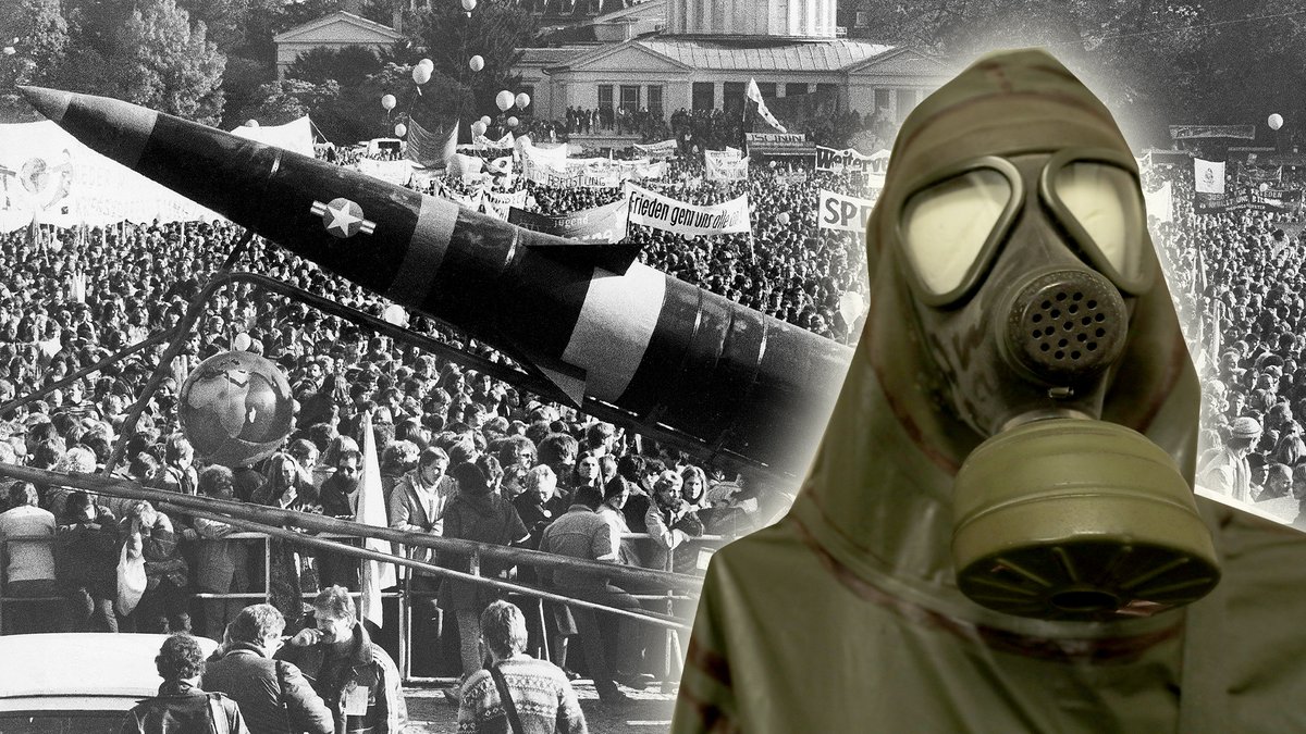 Gasmaske mit Schutz-Anzug, montiert vor Demontranten mit einem lebensgroßen Modell einer Pershing-II-Rakete