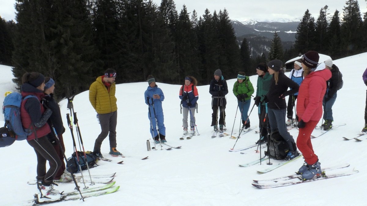 Eine Gruppe von Frauen steht auf einem Schneefeld im Halbkreis und hört der Trainerin zu. 