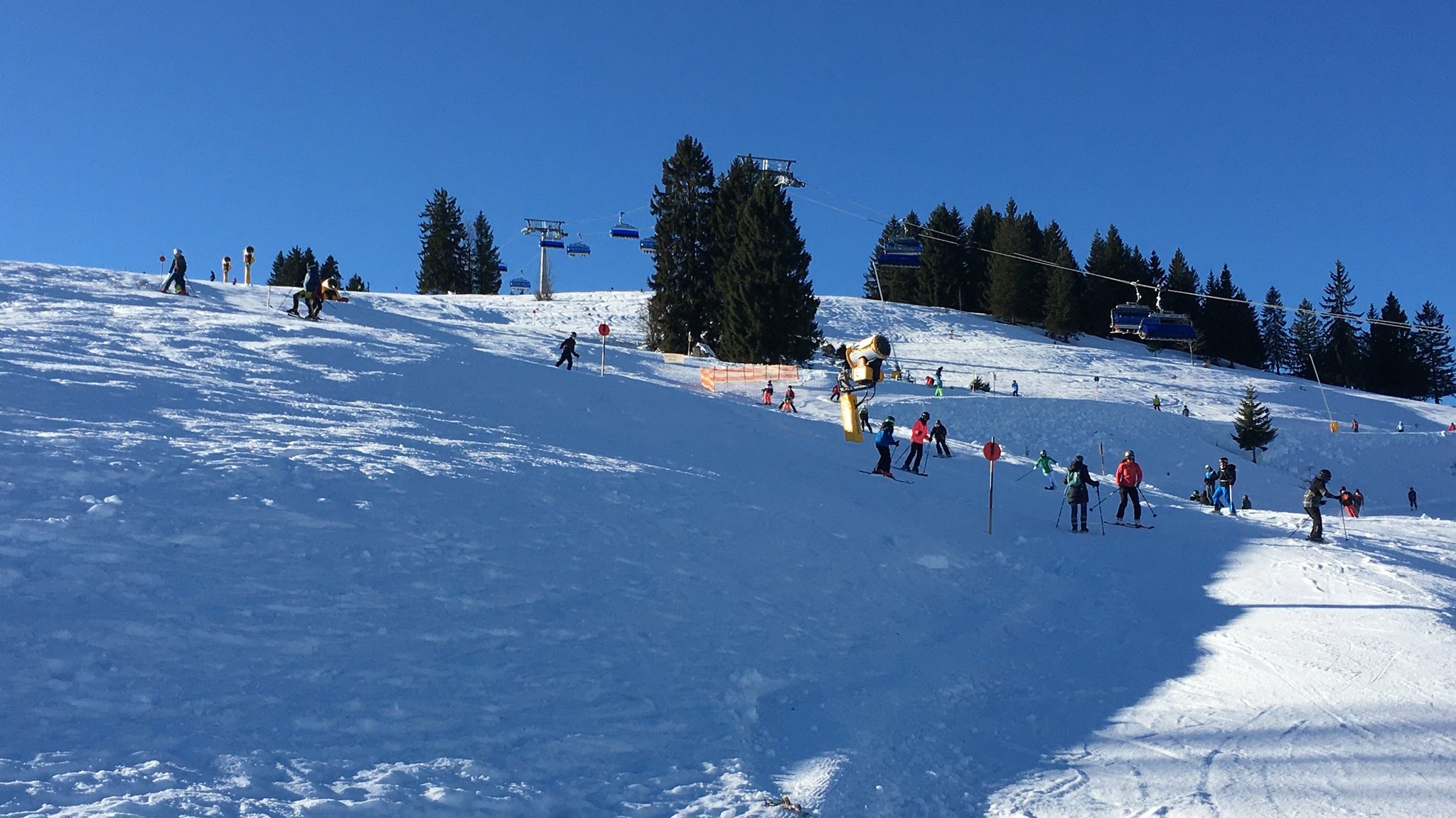 Vor blauem Himmel fahren etliche die Piste am Sudelfeld herunter. 