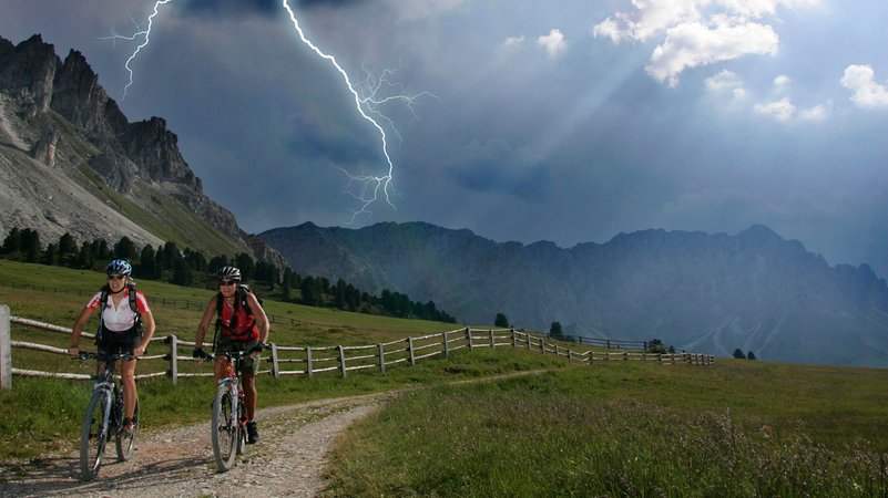 Zwei Fahrradfahrerinnen bei Blitz unterwegs in den Bergen