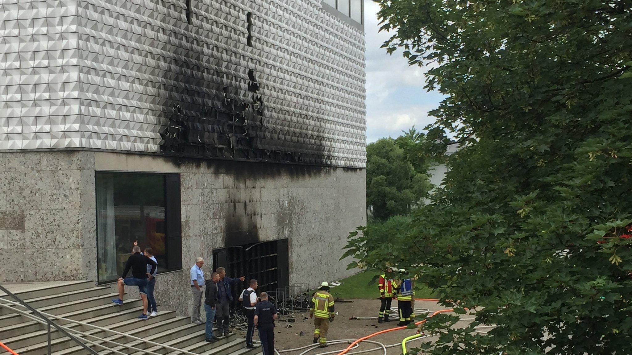 Mehrere Menschen - unter ihnen Feuerwehrmänner und Sachverständige - stehen vor der stark beschädigten und verrußten Kirchenfassade in Poing.