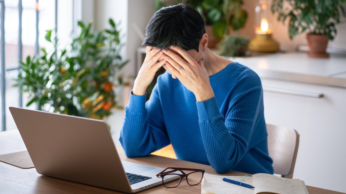 Eine Frau im blauen Pullover sitzt vor einem Laptop und stützt den Kopf in die Hände | Bild: picture alliance / Zoonar | Dmitrii Marchenko Eine Frau im blauen Pullover sitzt vor einem Laptop und stützt den Kopf in die Hände