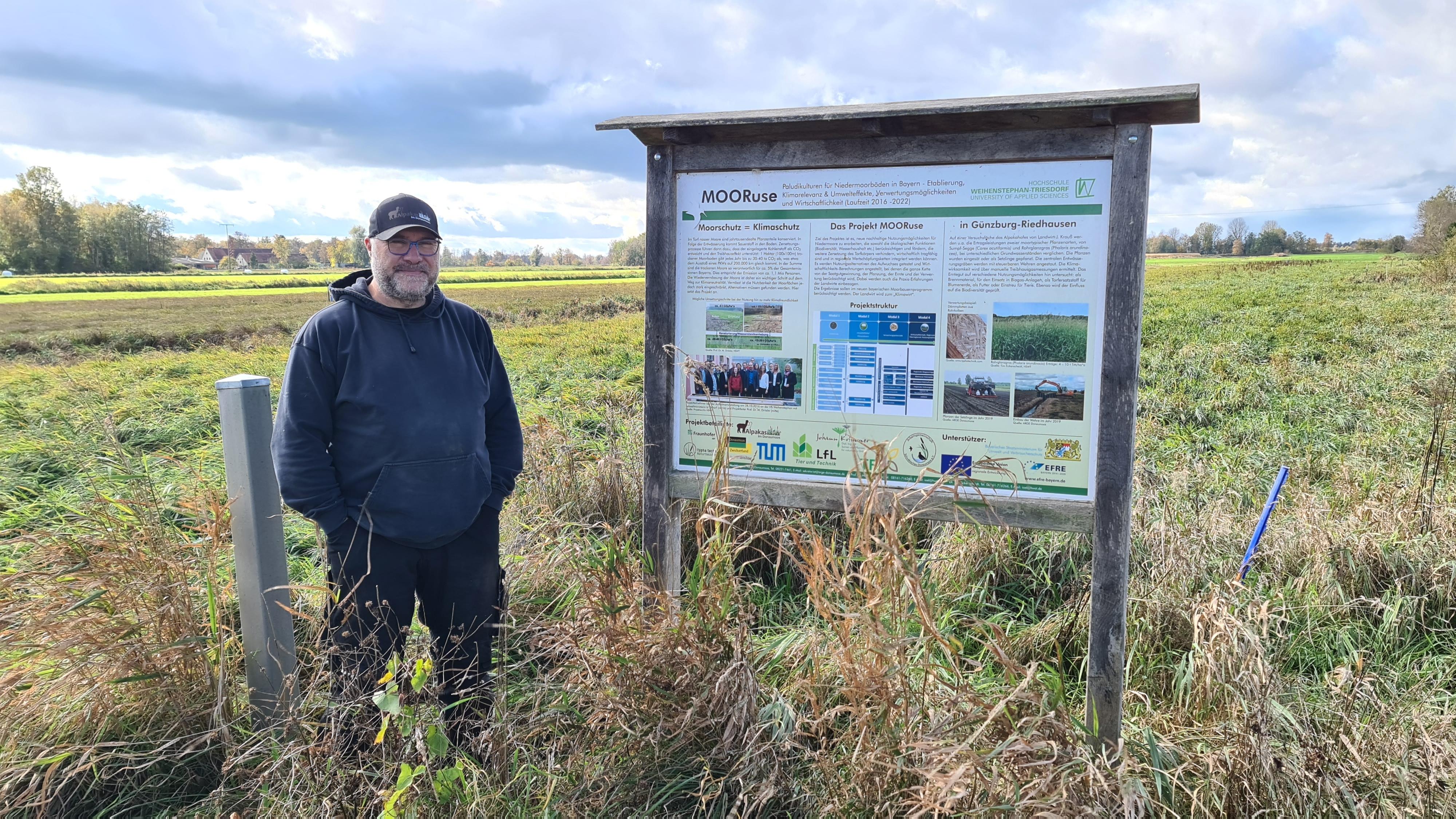 Mann steht auf einem Feld mit hohem Gras und einer Infotafel.
