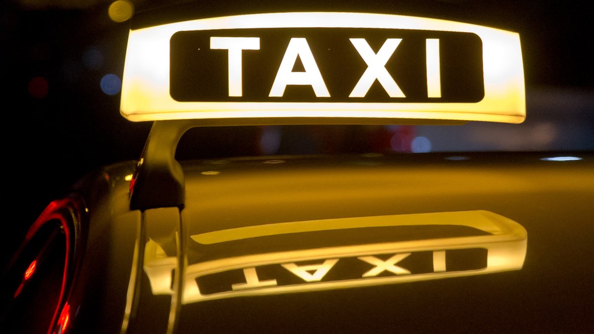 Ein beleuchtetes Taxi-Schild auf einem Autodach.