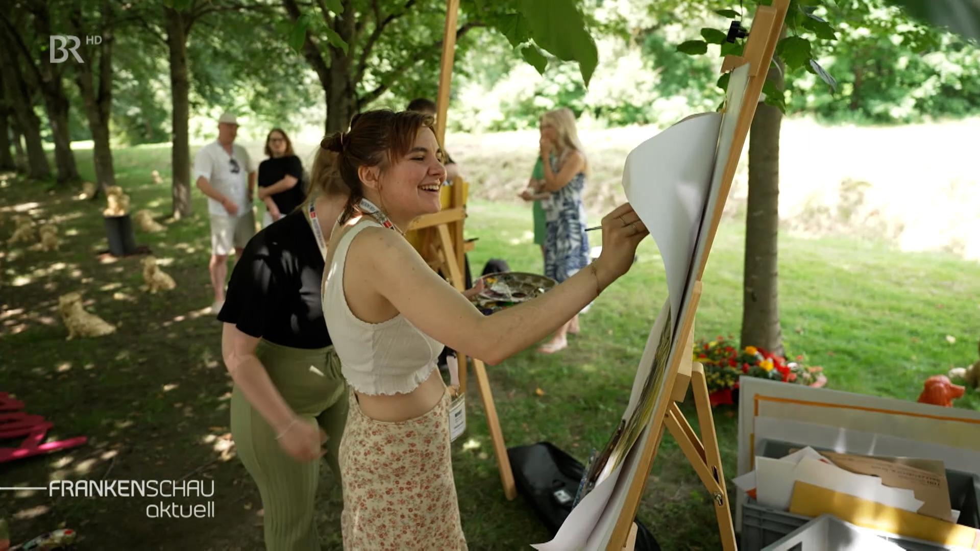 Männer und Frauen malen im Freien unter einer Allee.