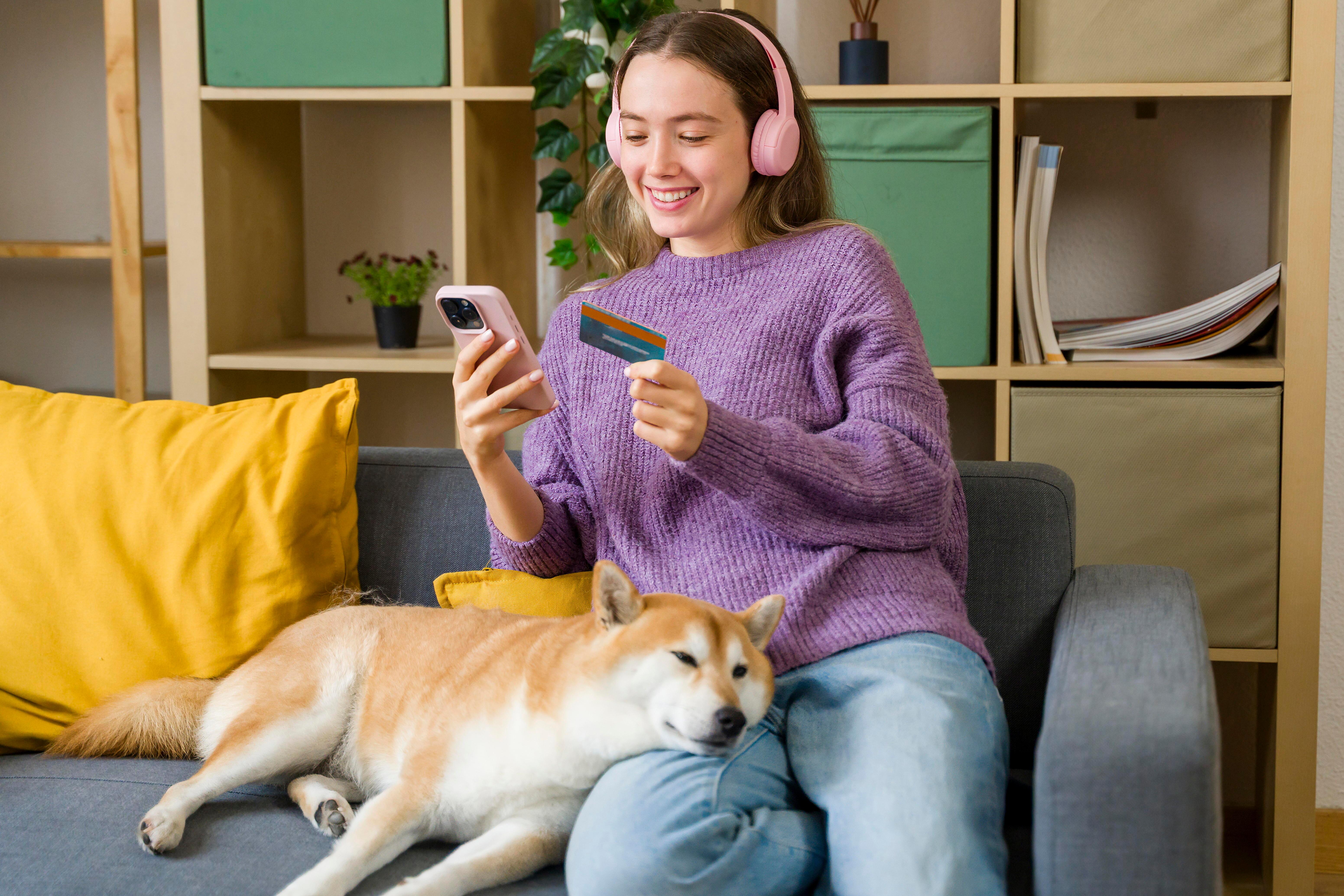 Junge Frau sitzt auf Sofa und kauft am Handy ein