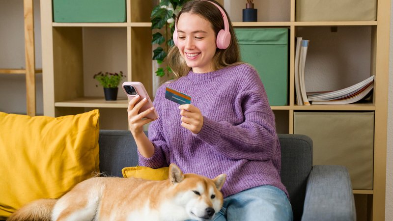 Junge Frau sitzt auf Sofa und kauft am Handy ein | Bild: dpa picture alliance / Westend61 / cocoon studio Junge Frau sitzt auf Sofa und kauft am Handy ein