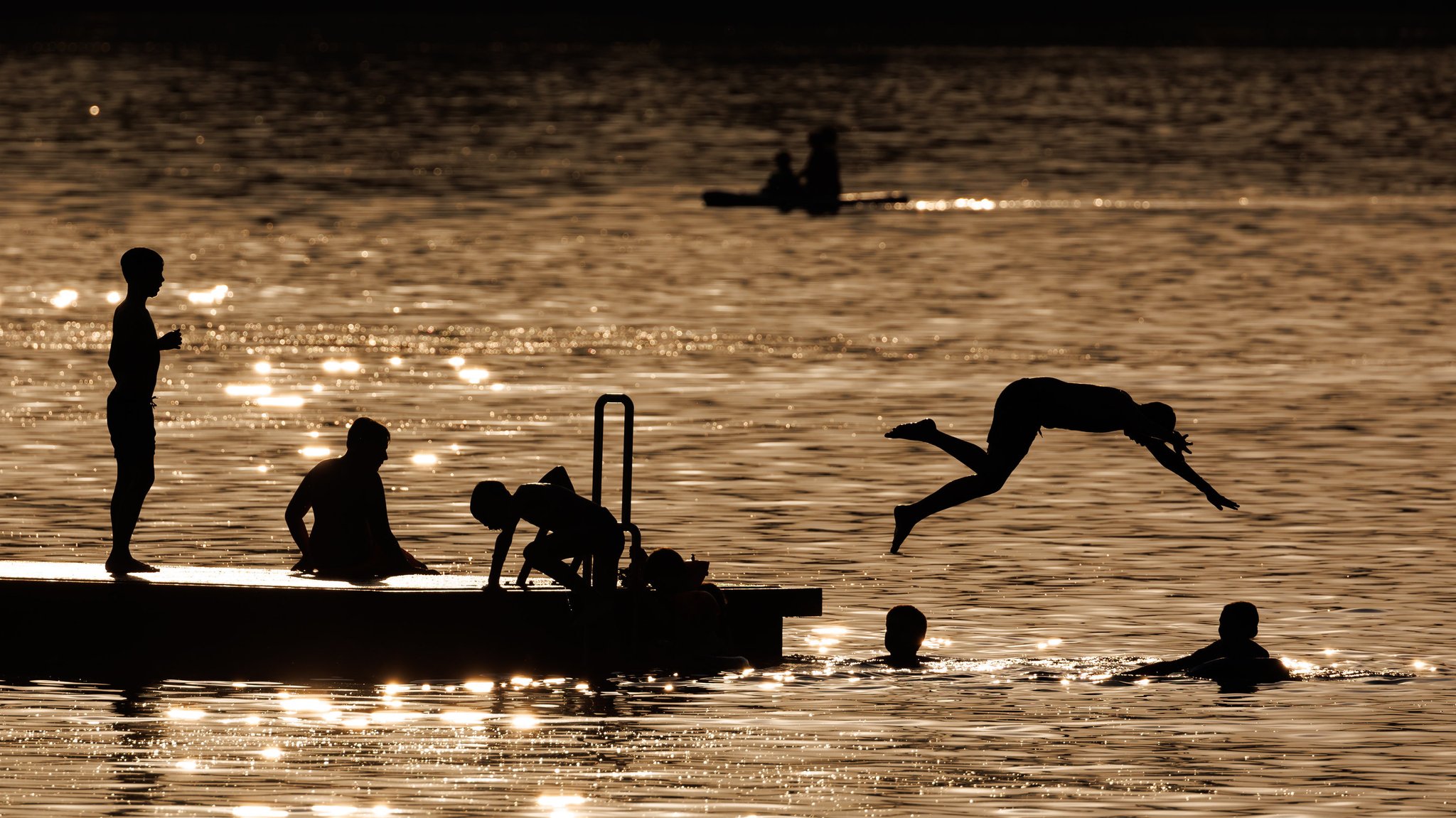 Badende springen am Abend von einem Schwimmsteg in den Igelsbachsee im Landkreis Weißenburg-Gunzenhausen