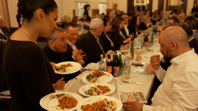 An langen Tischen werden Teller aufgetragen beim interreligiösen Fastenbrechen in München | Bild: Bayerischer Rundfunk 2025 An langen Tischen werden Teller aufgetragen beim interreligiösen Fastenbrechen in München