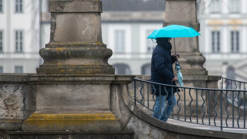 Eine Person geht mit einem aufgespanntem Regenschirm über eine Brücke