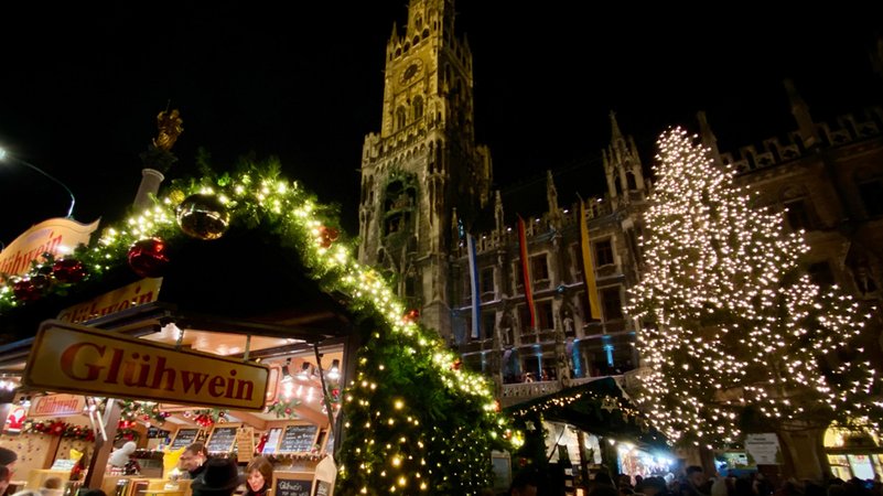 Beleuchteter Glühweinstand und Christbaum am Christkindlmarkt am Münchner Marienplatz.
