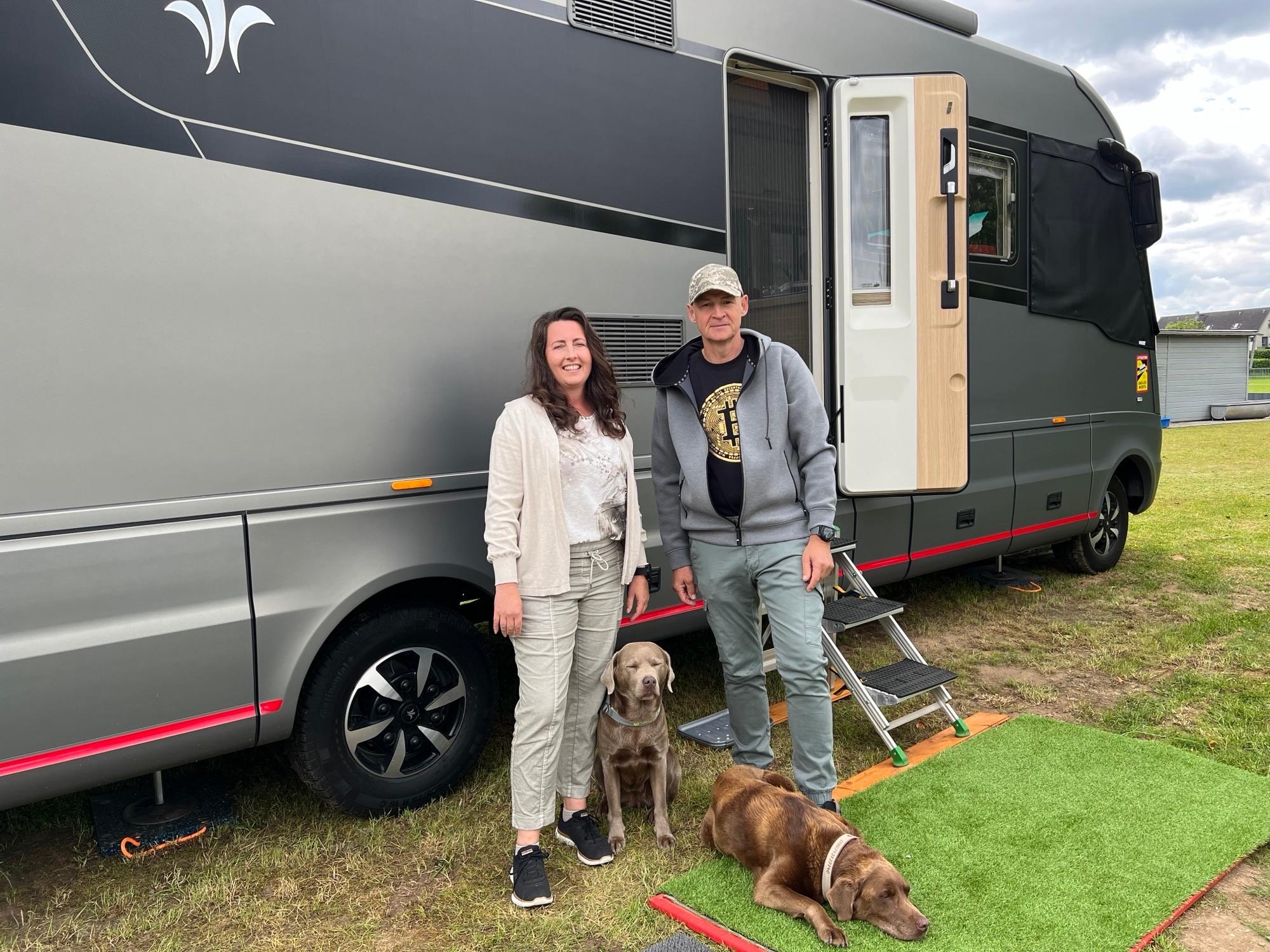 Das Ehepaar Melanie und Martin Ebert steht mit seinen beiden Hunden vor einen großen, grauen Wohnmobil. 