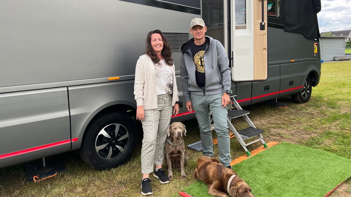 Das Ehepaar Melanie und Martin Ebert steht mit seinen beiden Hunden vor einen großen, grauen Wohnmobil. 