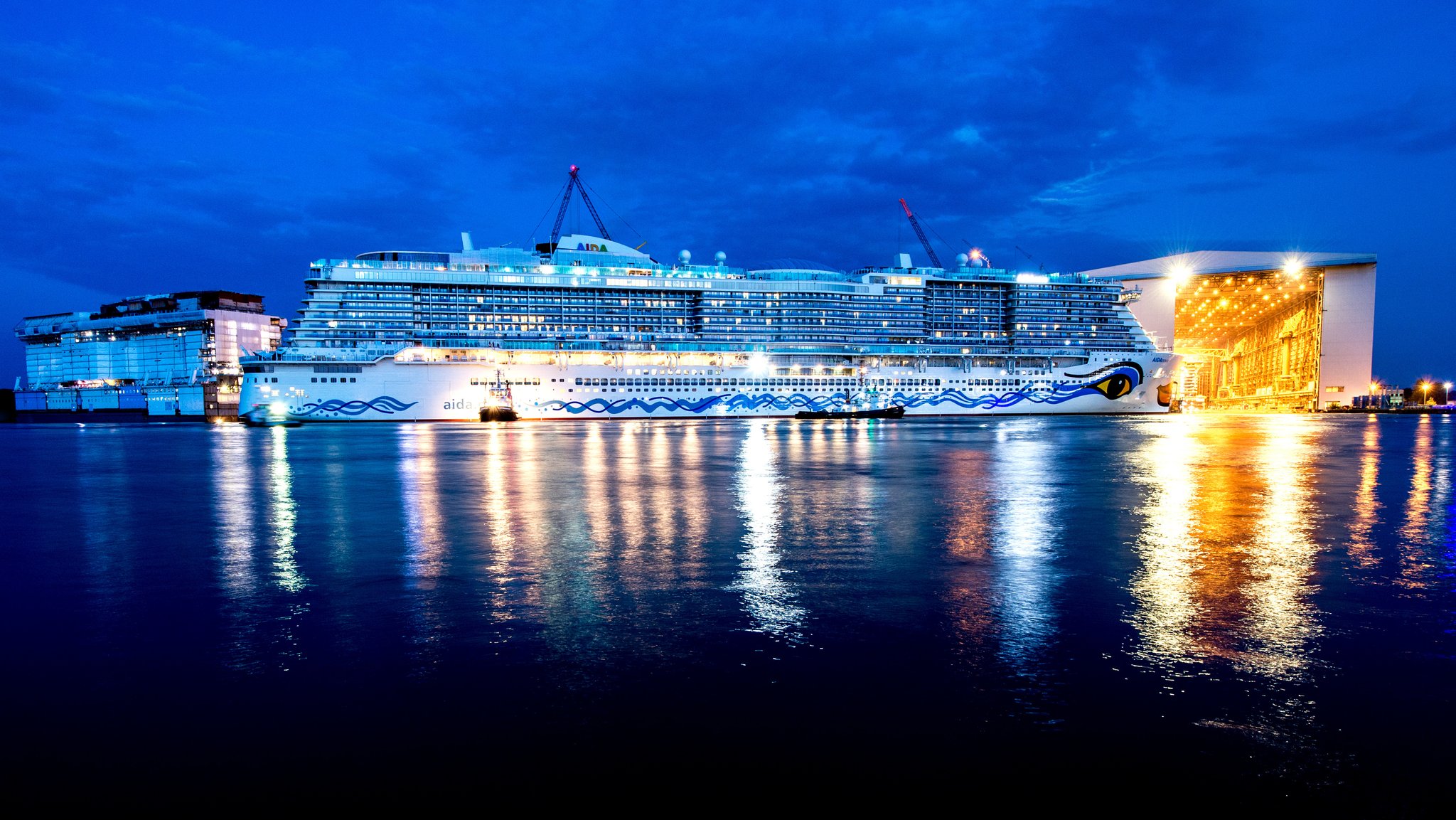 Schlepper ziehen im Jahr 2018 das neue Kreuzfahrtschiff Aidanova aus der überdachten Werfthalle der Meyer-Werft