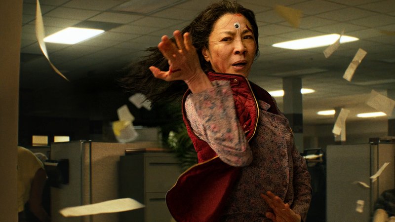 Filmbild aus "Everything Everywhere All At Once": Eine Frau in heftiger Bewegung in einer Büroetage, durch die Papiere fliegen