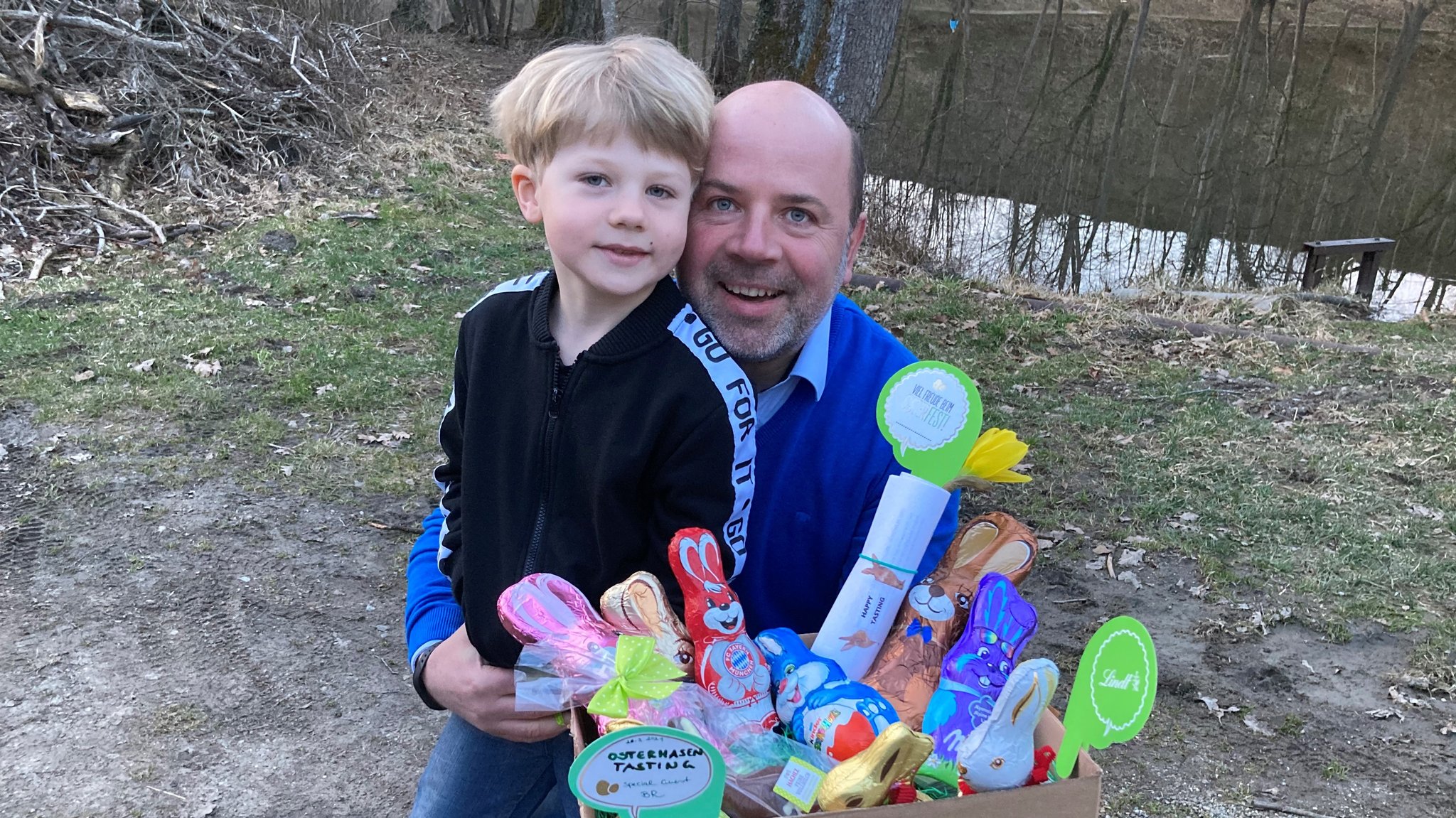 Karsten Riedel und sein Sohn Ben, sechs Jahre, halten eine  Pappkiste mit 10 Schokoosterhasen  in den Händen. 