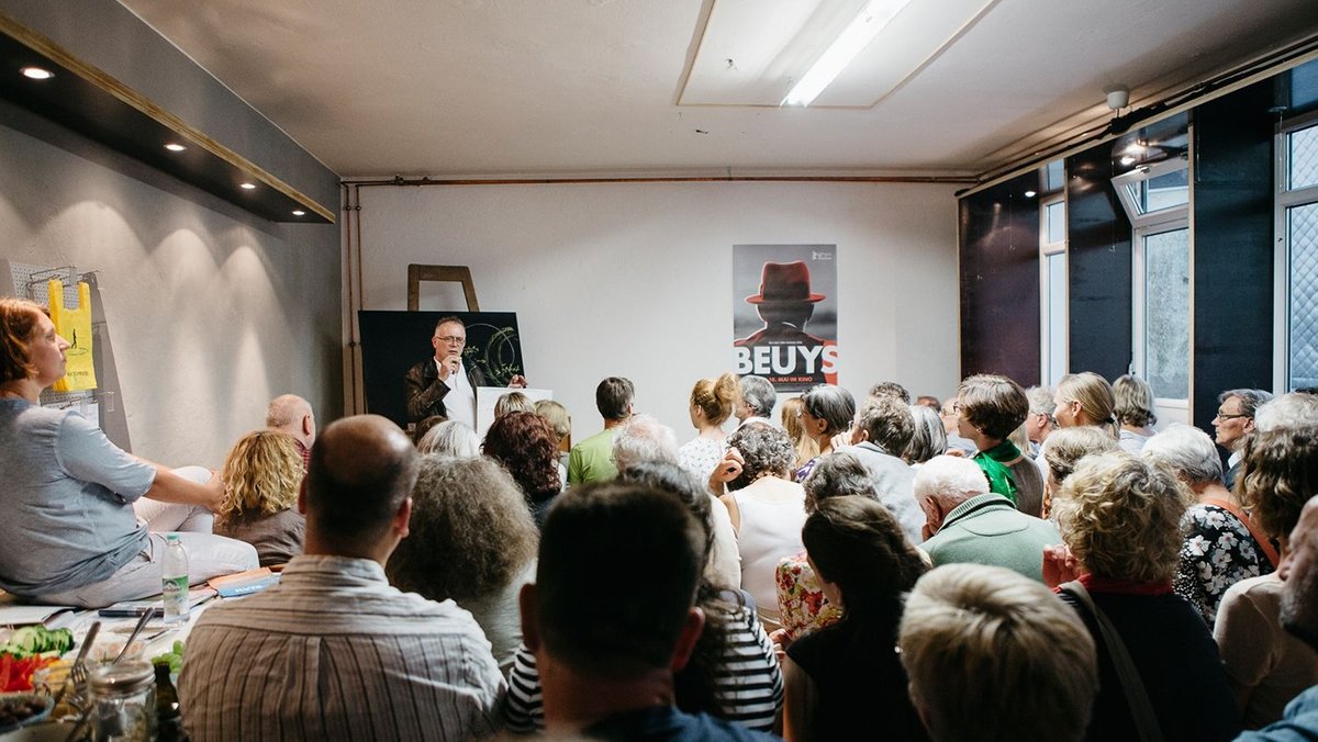 In einem vollen Atelier präsentiert ein ehemaliger Mitarbeiter von Joseph Beuys seine Arbeit.