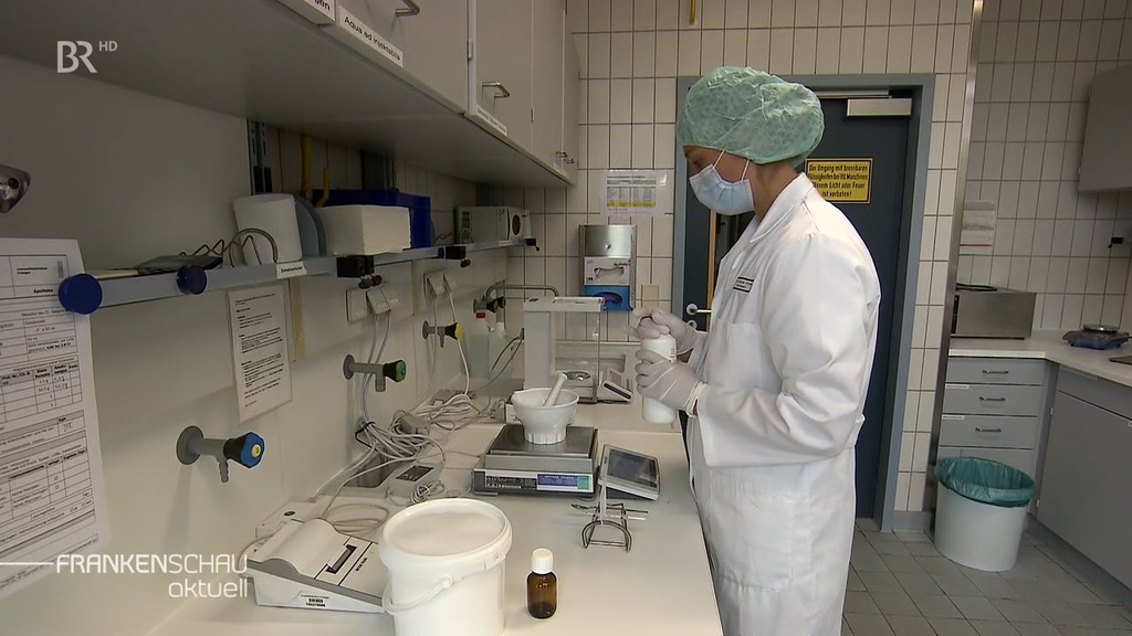 Eine Frau in weißem Kittel, mit Mundschutz und Haube hantiert in einem Labor.
