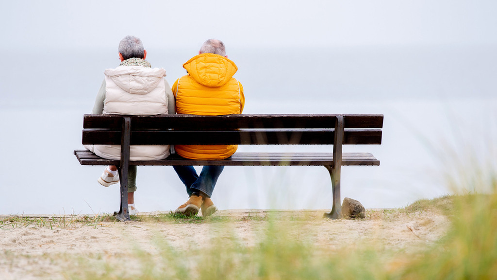 Touristen sitzen bei trübem Wetter auf einer Bank am Strand vor der Nordsee.
