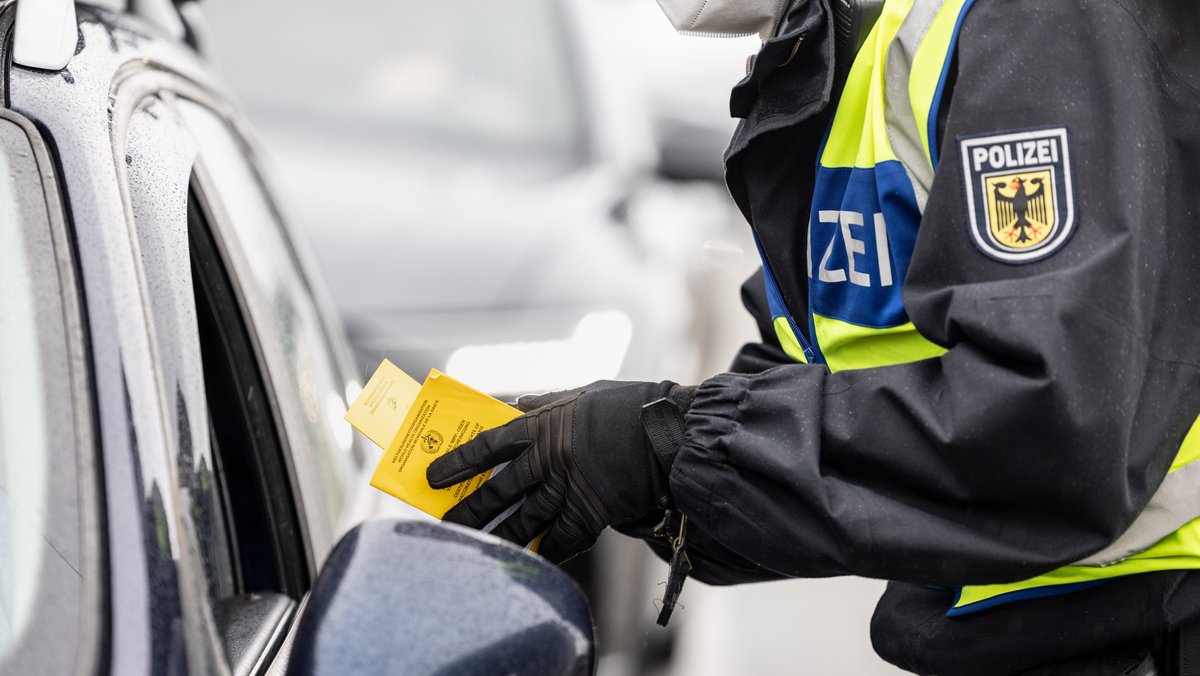 Ein deutscher Bundespolizist kontrolliert an der Grenze zu Österreich auf der Autobahn A93 den Impfpass einer einreisenden Person. 