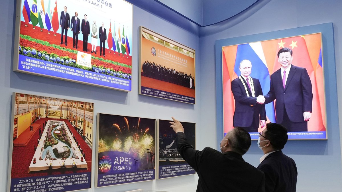 Zwei Besucher vor einem Bild, auf dem der chinesische Präsident Xi Jinping Wladimir Putin die Hand schüttelt