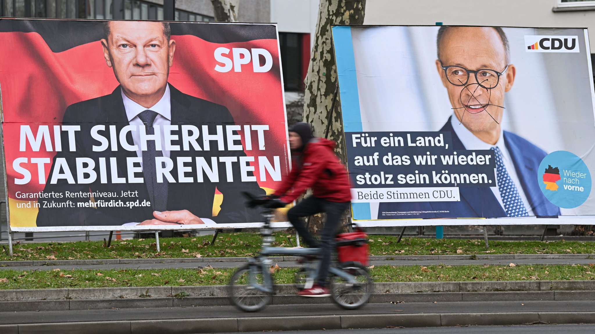  in Radfahrer fährt an zwei Wahlplakaten mit den Spitzenkandidaten von SPD und Union, Kanzler Olaf Scholz (l) und CDU-Chef Friedrich Merz, vorbei.