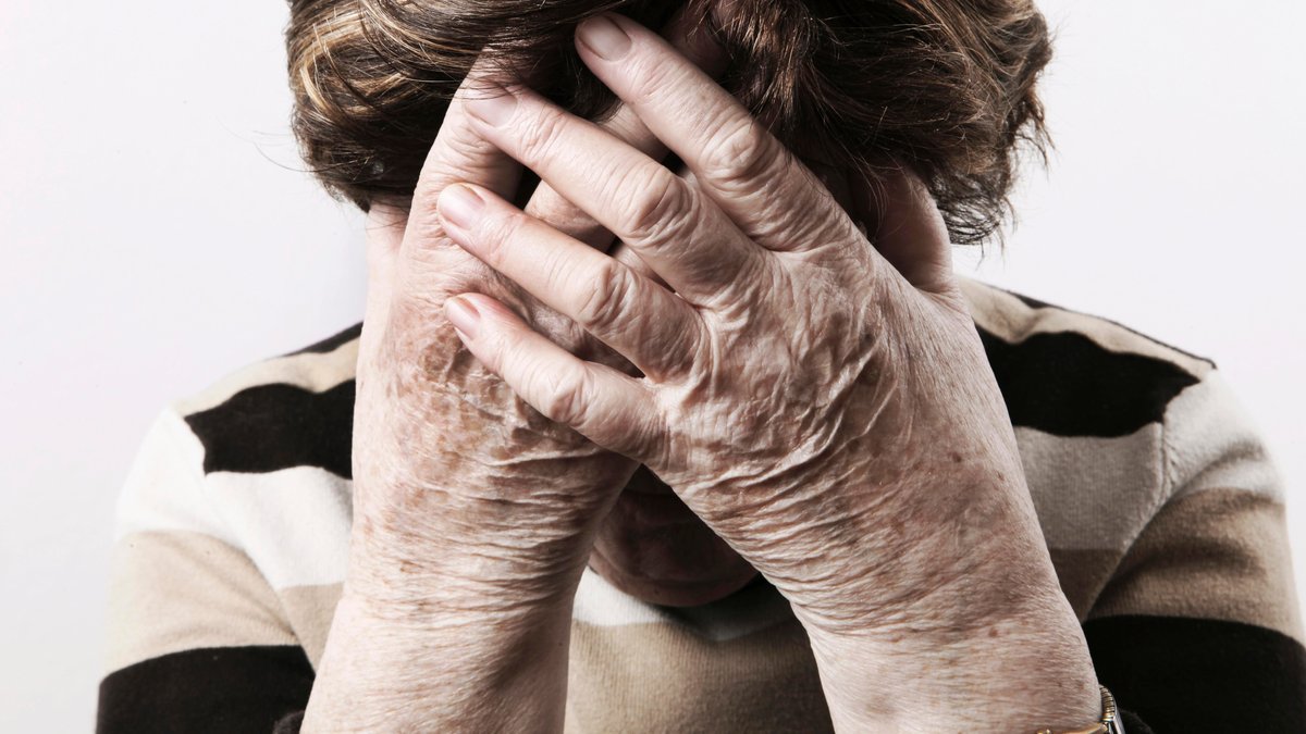 Eine ältere Frau hält die Hände vor ihr Gesicht.