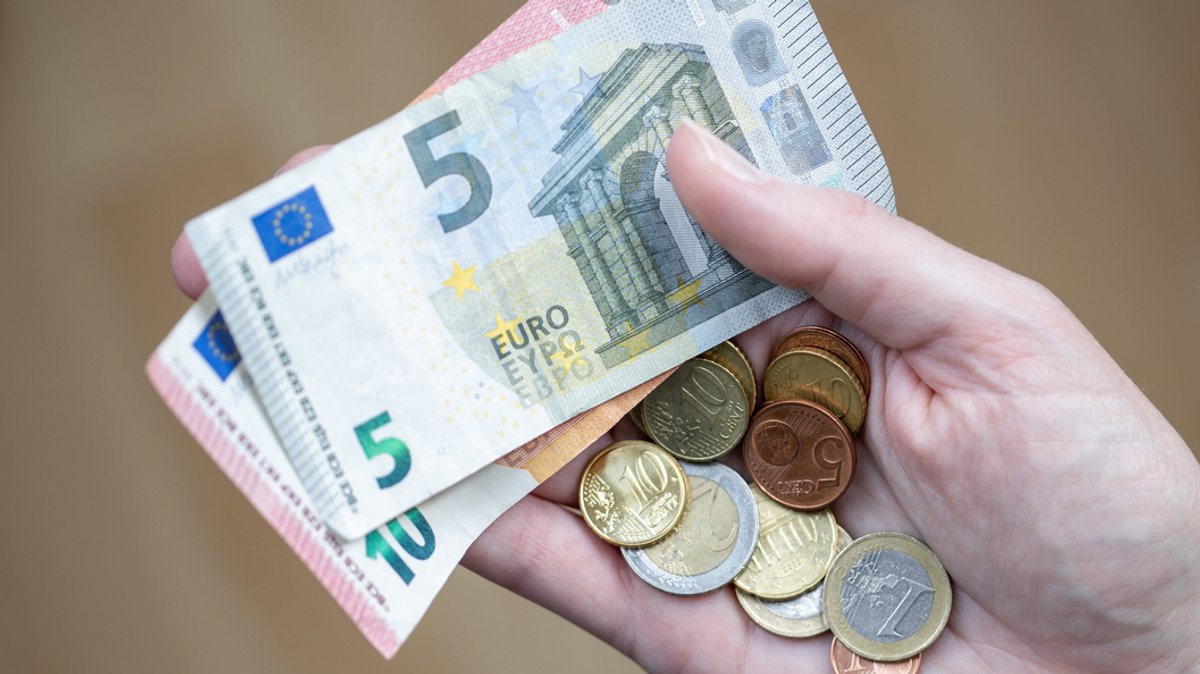 Eine Frau hält Euro-Geldscheine und Münzen in der Hand